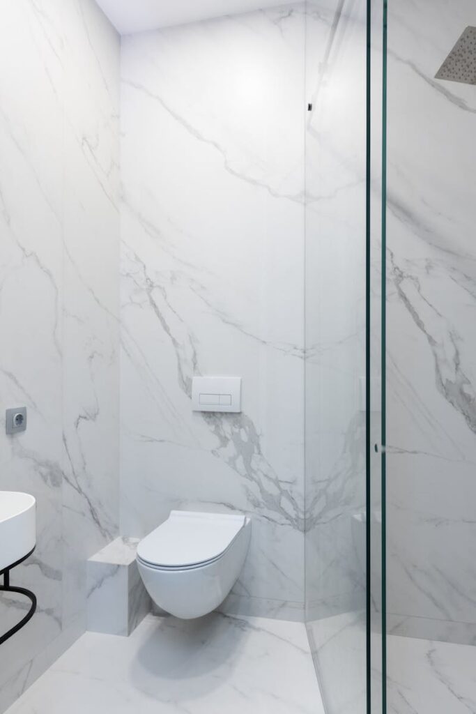 Elegant white marble bathroom featuring a sleek shower, toilet, and sink.
